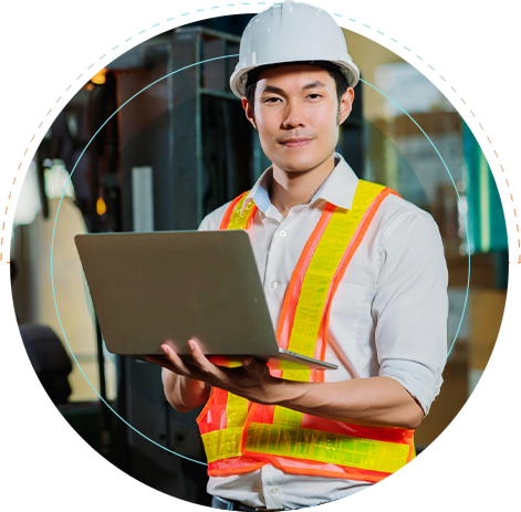 An outsourced engineering and construction professional at a worksite with a hardhat and high visibility jacket working on a computer